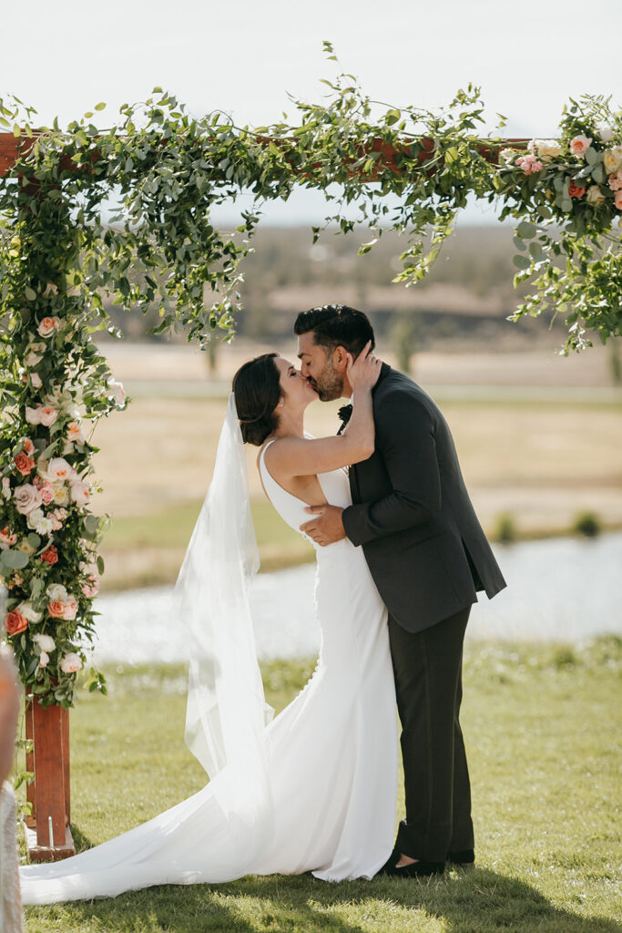 couples kiss under the arbor full of sophisticated florals and smilax